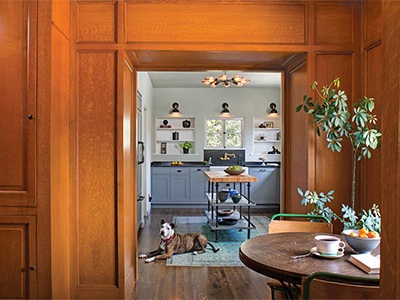 Small breakfast nook inside wood-paneled butler's pantry with remodeled Spanish-style kitchen and pet dog seen beyond