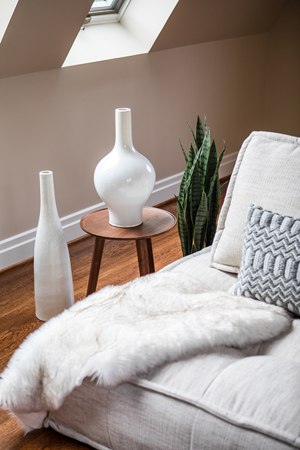 Contemporary living room detail with soft grey couch, wood side table with white vases, and house plant