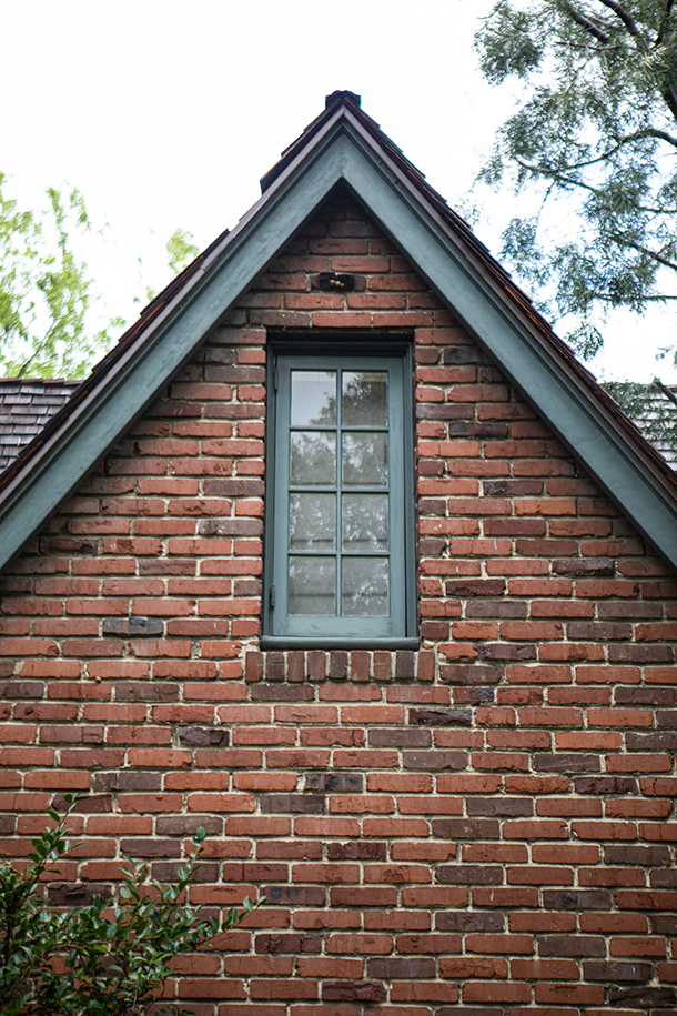 English cottage style home exterior A-frame roof detail with red brick wall, muted blue trim, and wood shingle roof