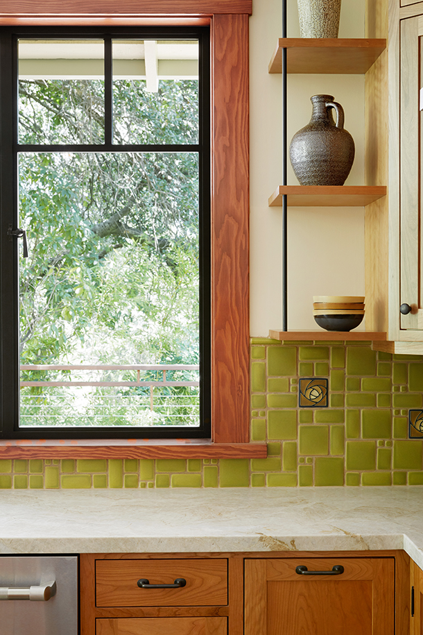 HartmanBaldwin Mira Monte Residence Kitchen Backsplash Detail Craftsman style kitchen remodel detail with wood and steel frame window, floating wooden shelves, cream stone countertop, stained wood cabinetry, and green tile backsplash with rosette accent tiles