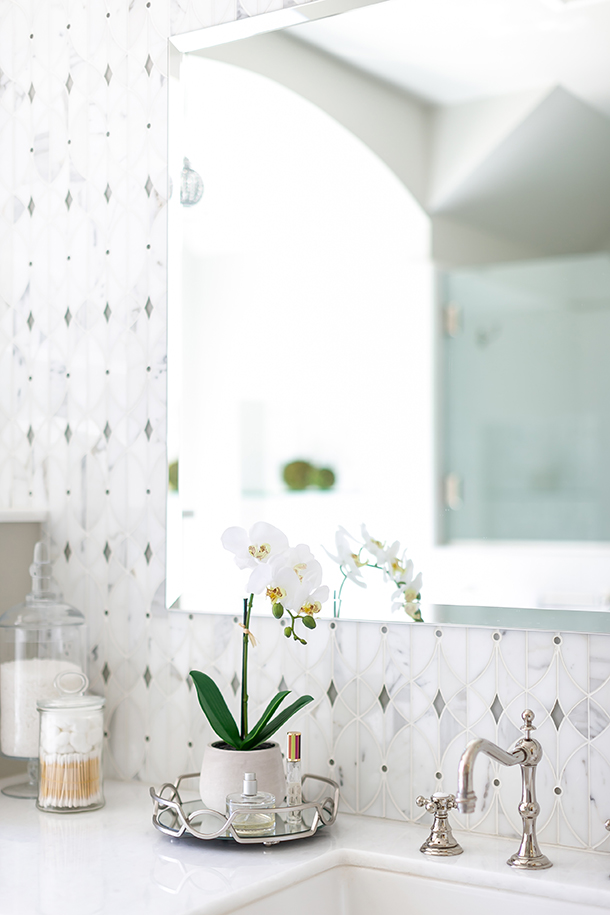 Elegant bathroom remodel detail with geometric pattern stone backsplash, white stone countertop, and polished nickel faucet