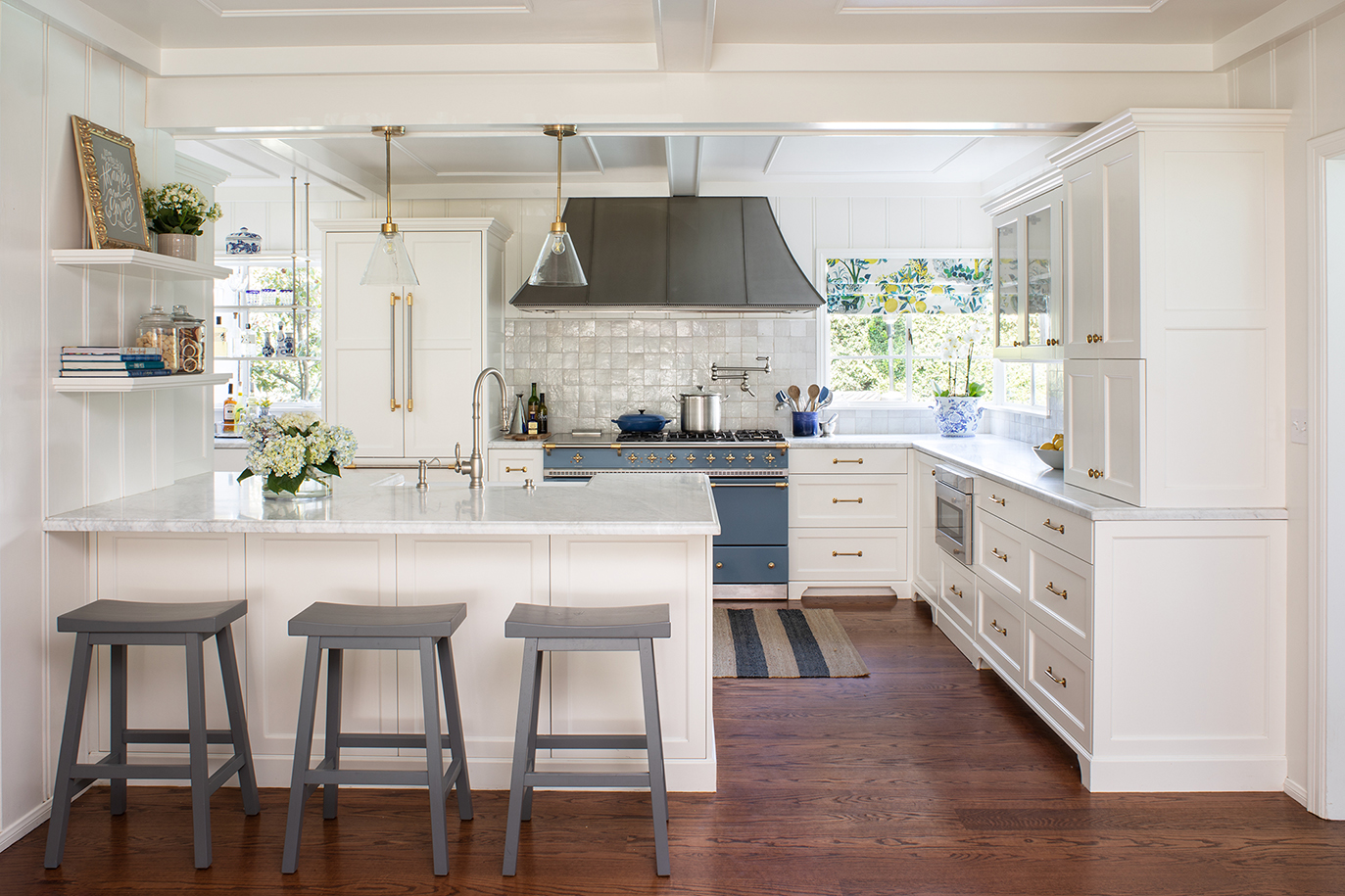Cape Cod style kitchen makeover with white cabinetry, spacious peninsula, blue French Lacanche range, and mixed-metal hardware