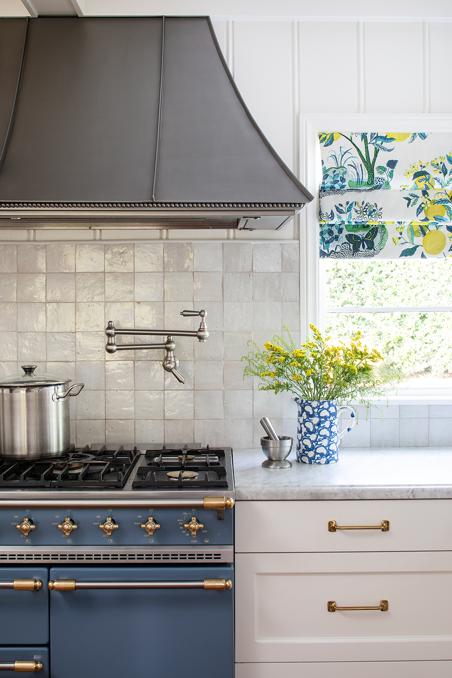 Cape Cod coastal-inspired kitchen detail with Blue French Lacanche range, textured zellige backsplash tile, and aged brass hardware
