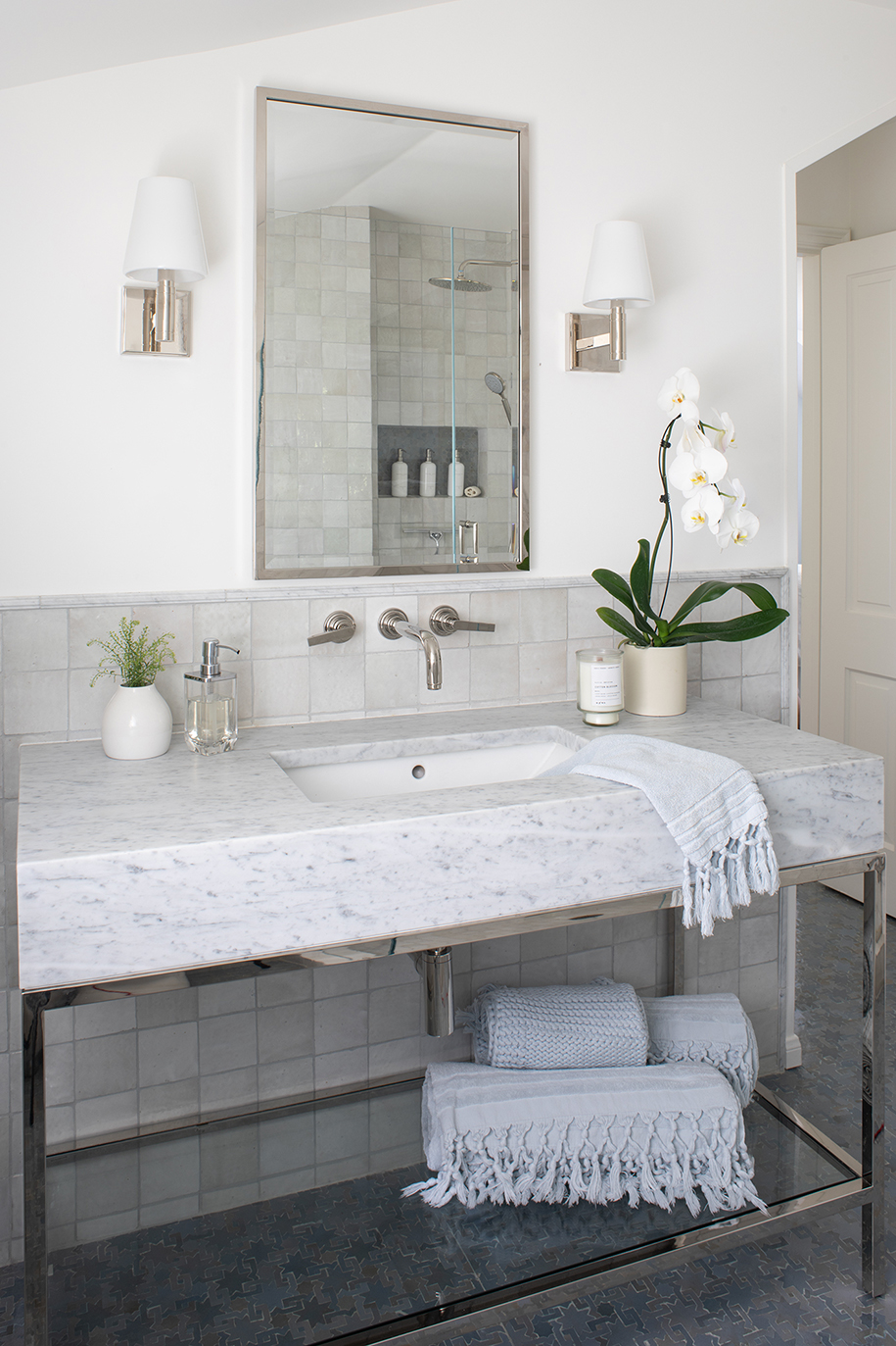 Cool-toned master bathroom with light grey zellige wall tiles, blue Moroccan mosaic flooring, and polished nickel and stone console sink