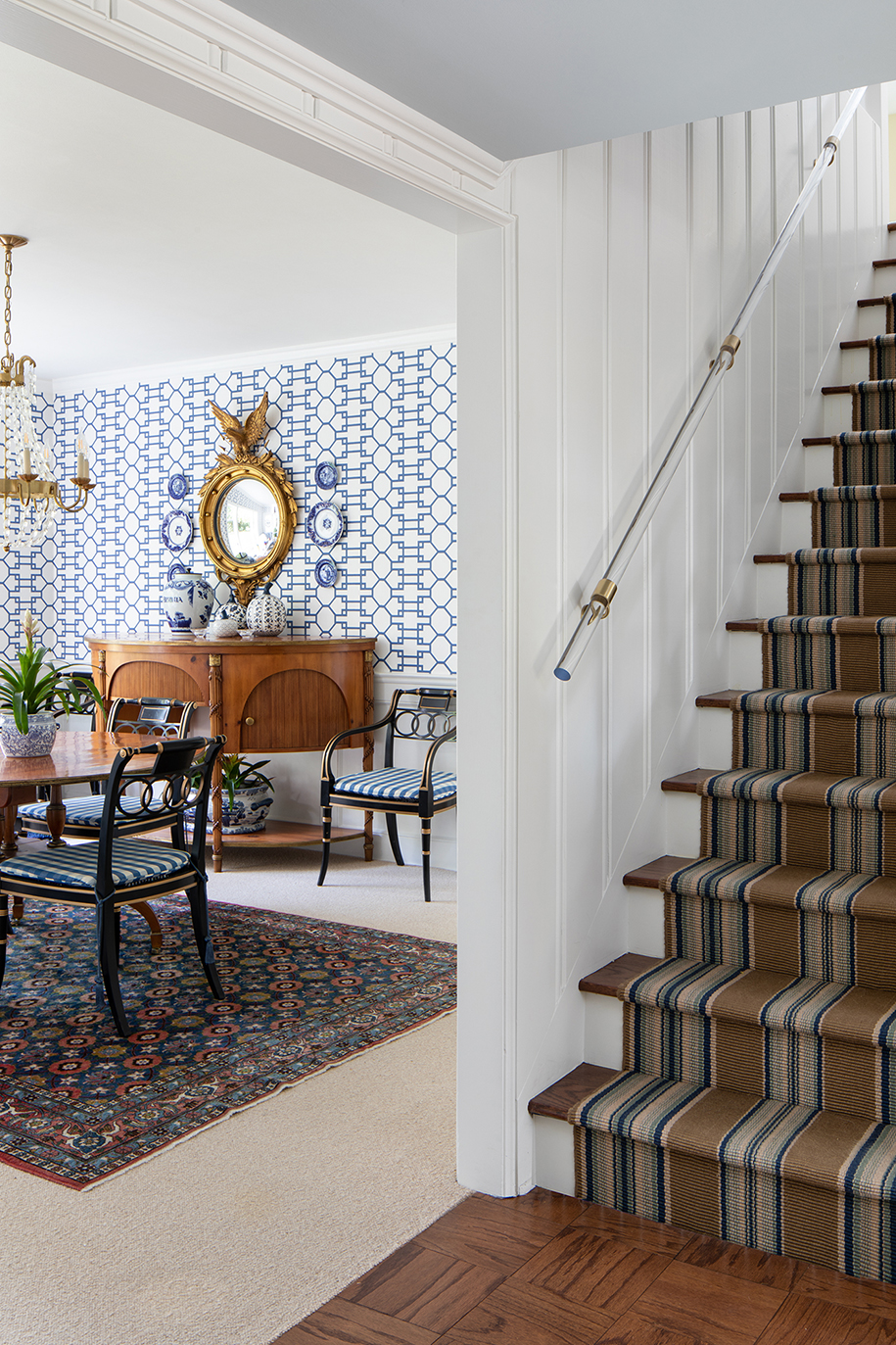 Cape Cod-style staircase and formal dining room with New England-inspired coastal patterns and design details in shades of blue, white, tan, and gold