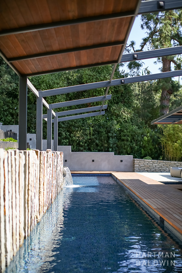 New luxury backyard lap pool with rock wall installation, waterfall, and retractable shade structure