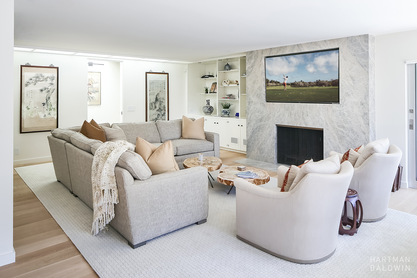 Remodeled contemporary living room with comfortable grey couches, live-edge wood coffee tables, and elegant light grey floor-to-ceiling granite wall that houses a fireplace and large TV