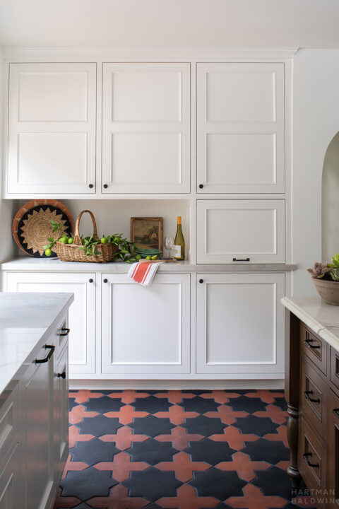 Functional white cabinetry in new Spanish style kitchen with contrasting red and black patterned terracotta floor