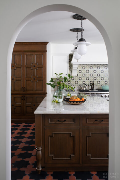 Spanish-style kitchen with colorful geometric tile, dark-stained woodwork, and wrought iron accents seen through arched doorway