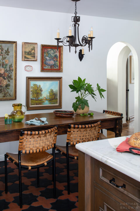 Spanish-style dining nook with dark wood table, colorful framed art, patterned tile flooring, and candelabra-inspired wrought iron lighting pieces
