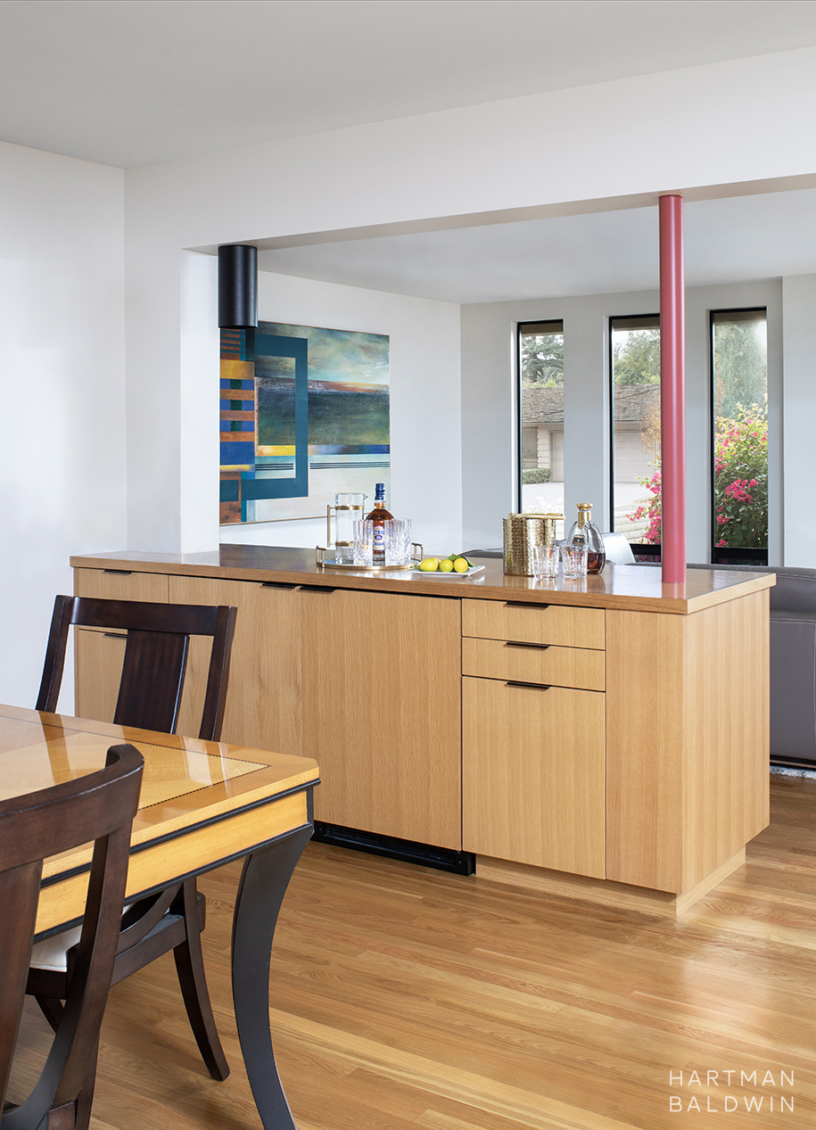Mid-Century Modern built-in wine refrigerator cabinet with slab-style oak cabinetry and red painted supportive column