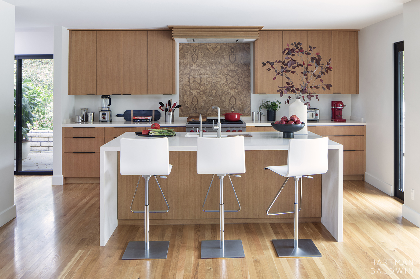 Mid-Century Modern kitchen renovation with waterfall-edge central island and bar seating, slab-style oak cabinetry, and book-matched wood veneer backsplash