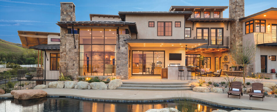 Pool view of large home with floor to ceiling windows, patio furniture, and water features.