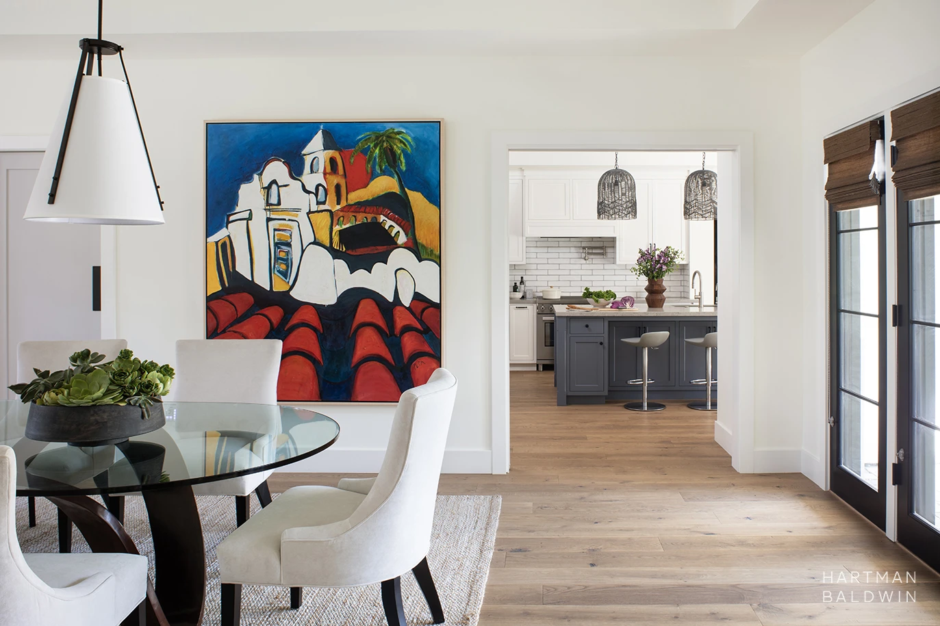 New custom modern dining room with a large colorful painting on the wall and the kitchen with white and blue cabinetry seen beyond