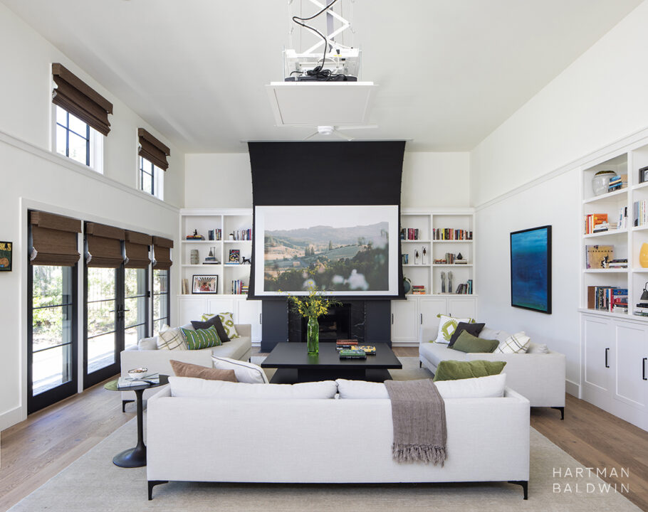 HartmanBaldwin Barrington Residence New Custom Modern Farmhouse Living Room Projector - Hartman Baldwin Pre-Launch Expansive great room with built-in bookshelves, wall-to-wall French doors, comfortable contemporary couches, and a retractable projector screen