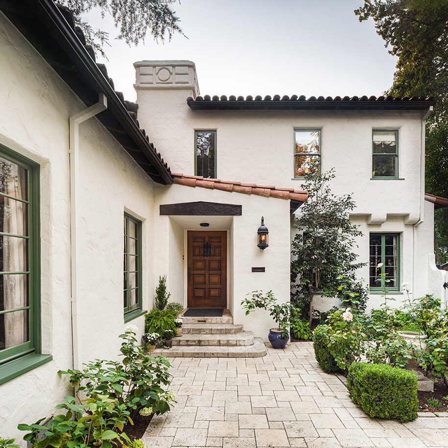 HartmanBaldwin Hill Residence Spanish Style Front Porch Crop - Hartman Baldwin Pre-Launch Front porch of a Spanish-style home with textured cream stucco walls, red-tile roof, green trim, and courtyard garden