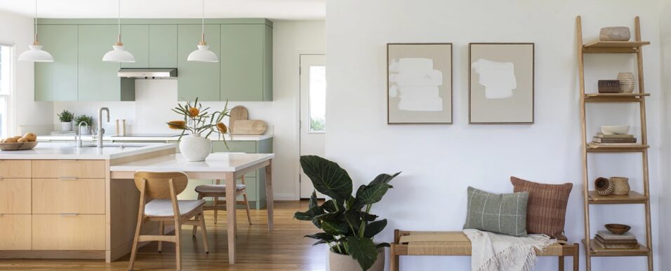 Entryway with neutral furnishings, art, and accessories. Contemporary Scandinavian minimalist style kitchen seen beyond with sage green cabinetry and island with built-in dining table