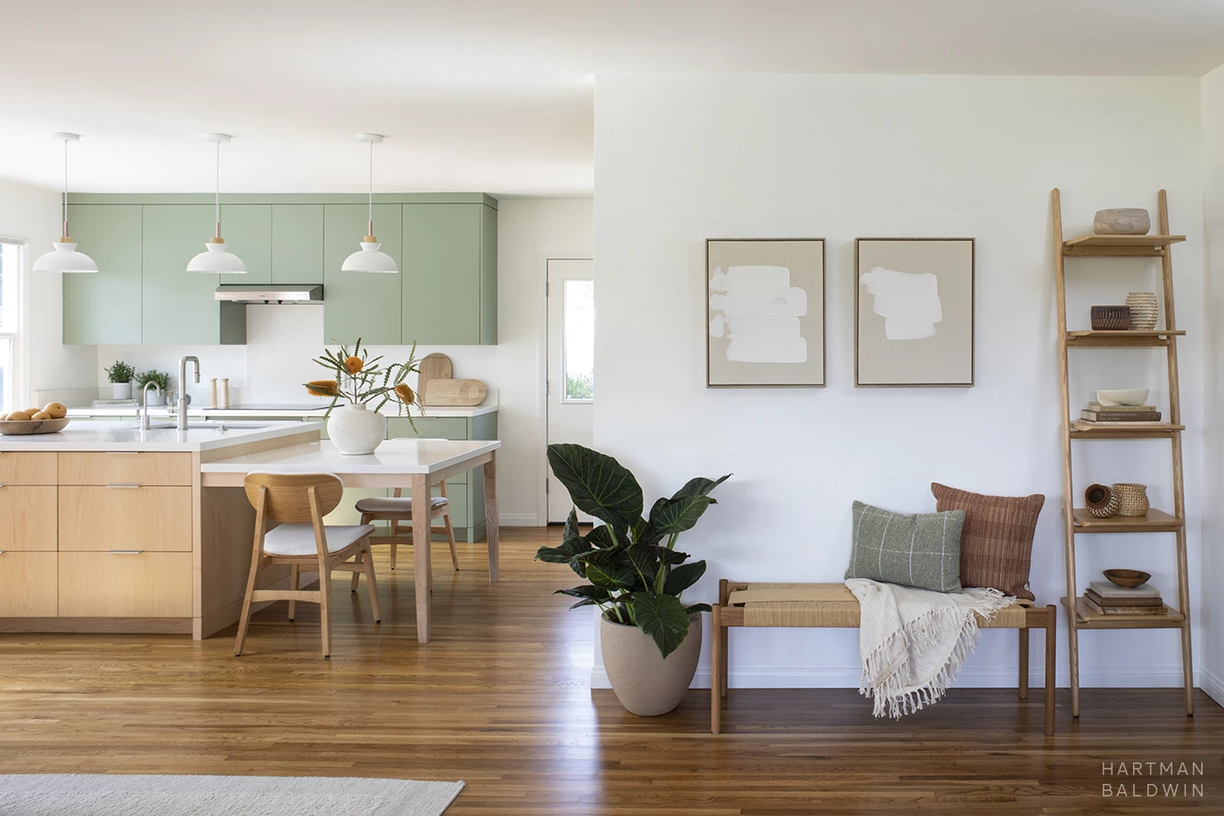 Entryway with neutral furnishings, art, and accessories. Contemporary Scandinavian minimalist style kitchen seen beyond with sage green cabinetry and island with built-in dining table
