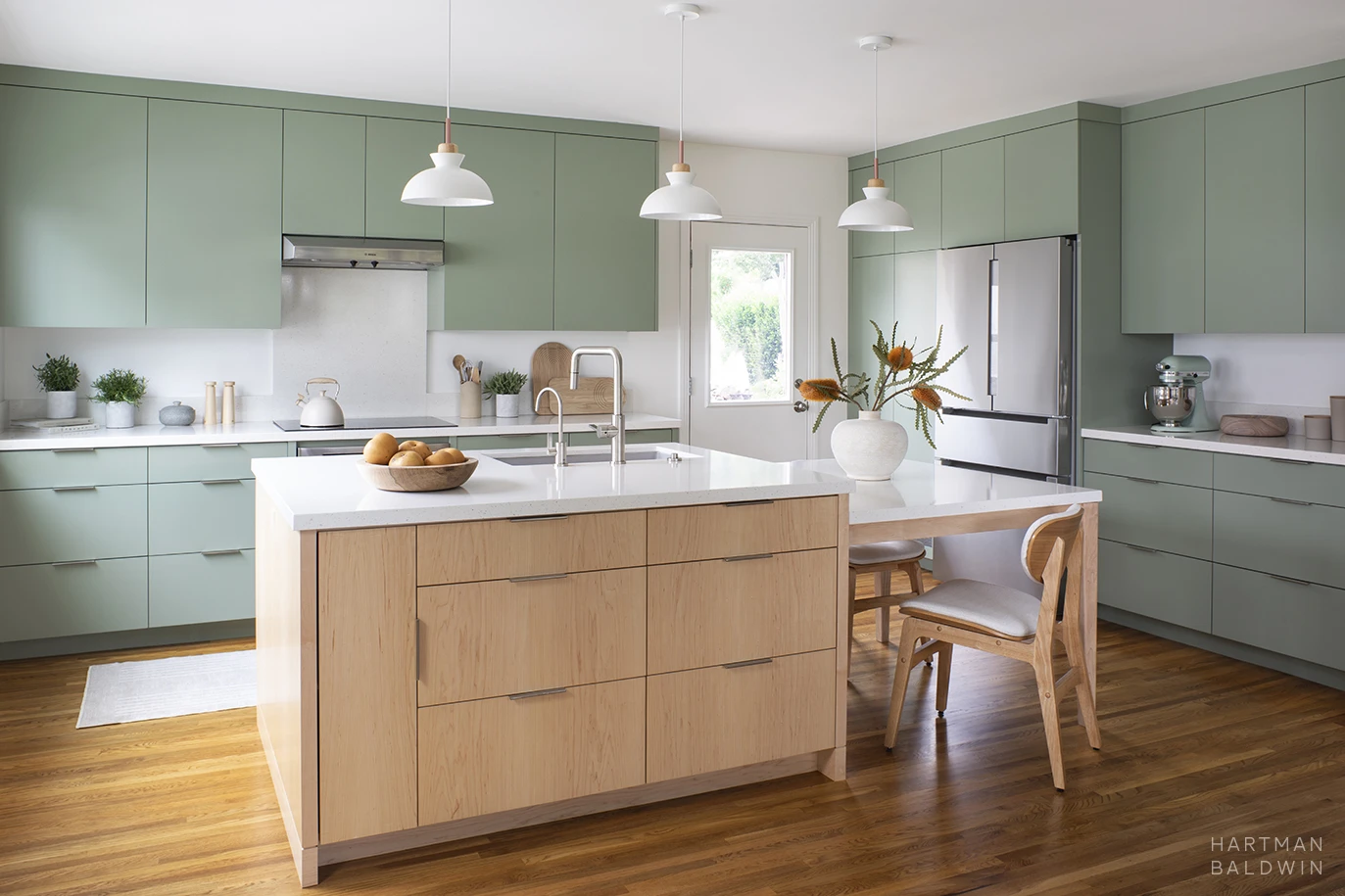 Contemporary Scandinavian minimalist style kitchen remodel with sage green cabinetry, sculptural pendant lights, and central island with built-in dining table