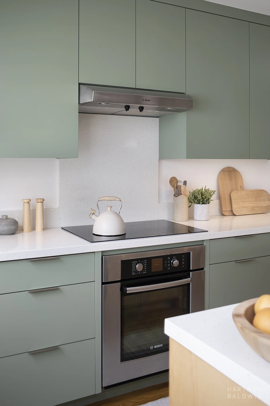 Scandinavian minimalist-style kitchen with sage green slab-style cabinetry, white quartz countertops, induction cooktop, minimalist vent hood, and Bosch oven