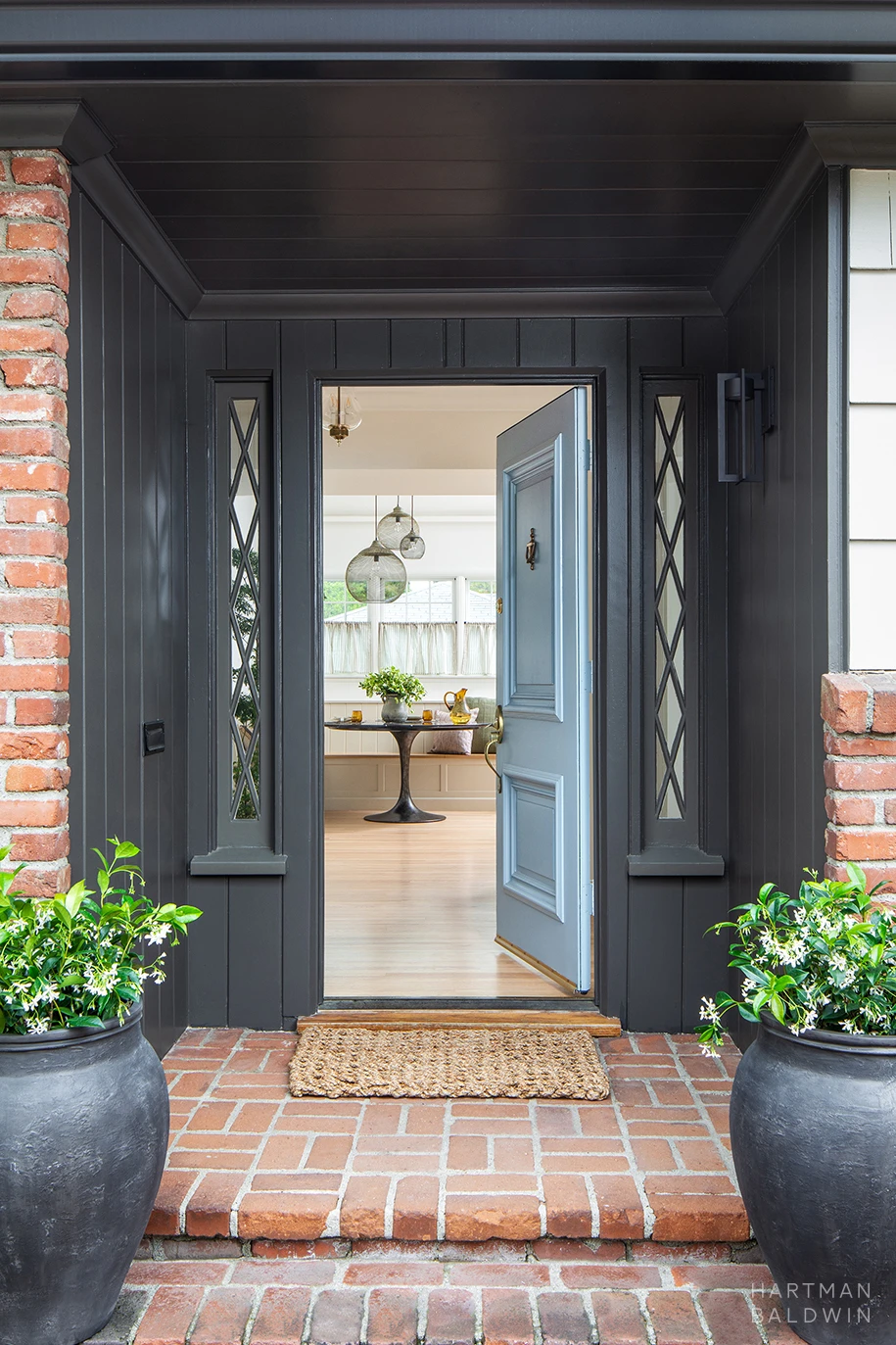 HartmanBaldwin Cambridge Residence California Ranch-Style Remodel Front Porch Remodeled front porch with red brick exterior, dark grey painted wood paneling, and blue front door open to entryway and breakfast nook inside