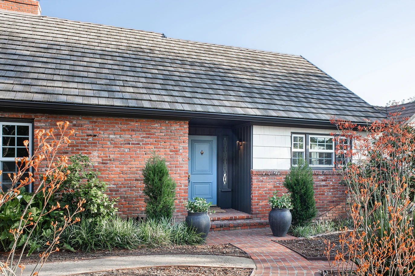 HartmanBaldwin Cambridge Residence California Ranch-Style Remodel Front Exterior California ranch-style home front exterior with red brick walls and blue-painted front door