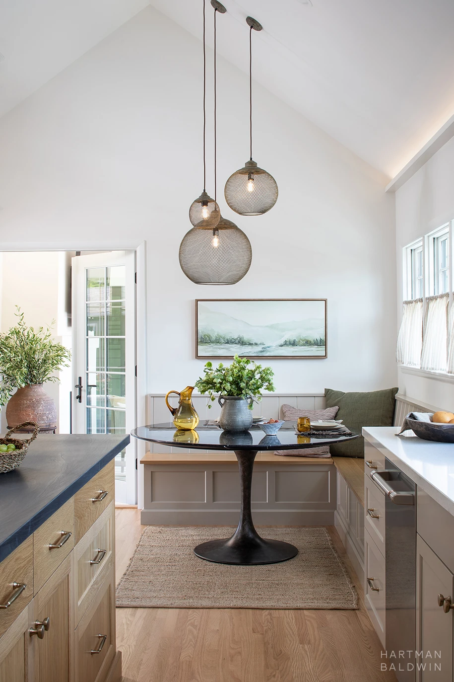 HartmanBaldwin Cambridge Residence California Ranch-Style Remodel Breakfast Nook Breakfast nook with built-in banquette bench, round dark stone table, hanging mesh pendant lights, and vaulted ceiling