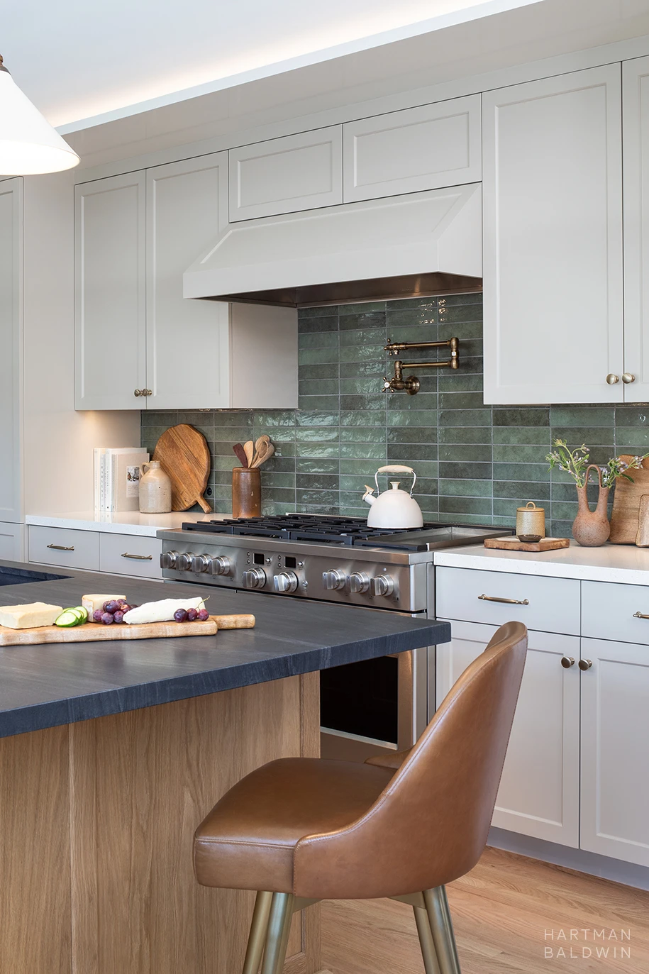 HartmanBaldwin Cambridge Residence California Ranch-Style Remodel Kitchen Range Remodeled kitchen detail with wood and dark stone island, tan-painted cabinetry, and stainless steel range with blue-green tile backsplash