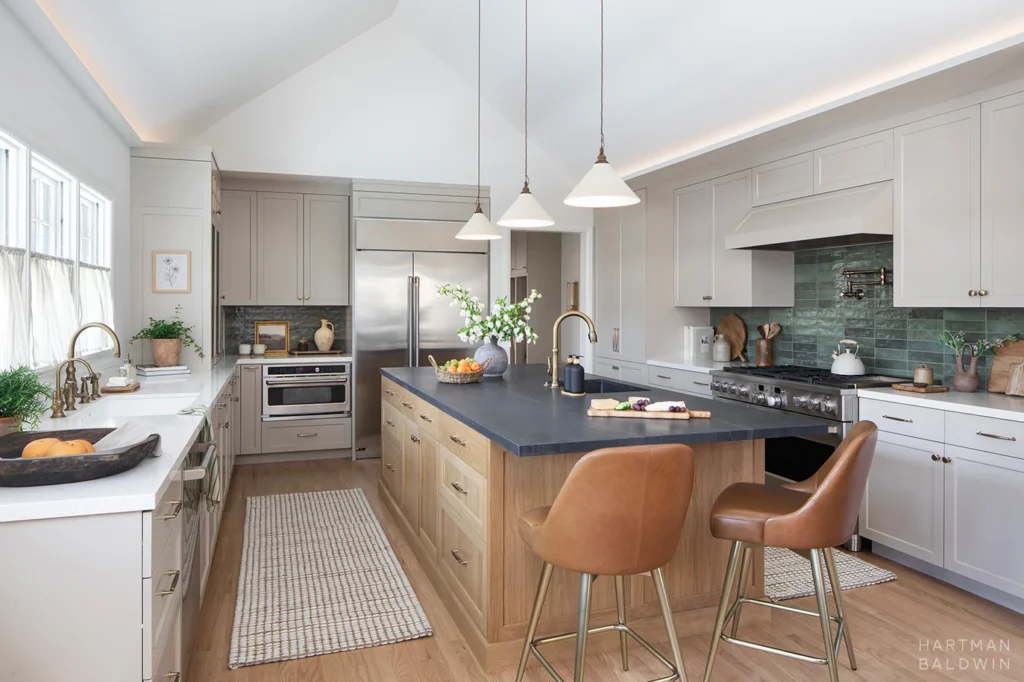 Contemporary kitchen remodel with wood and dark stone island, tan perimeter cabinetry, dark turquoise tile backsplash, and vaulted ceiling with cove lighting