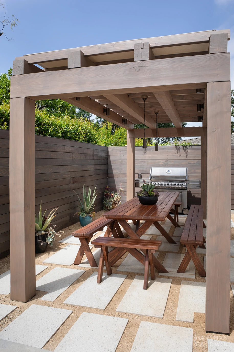 HartmanBaldwin Cambridge Residence California Ranch Backyard Pergola Backyard wooden shade structure with picnic table, cement pavers, and stainless steel barbecue