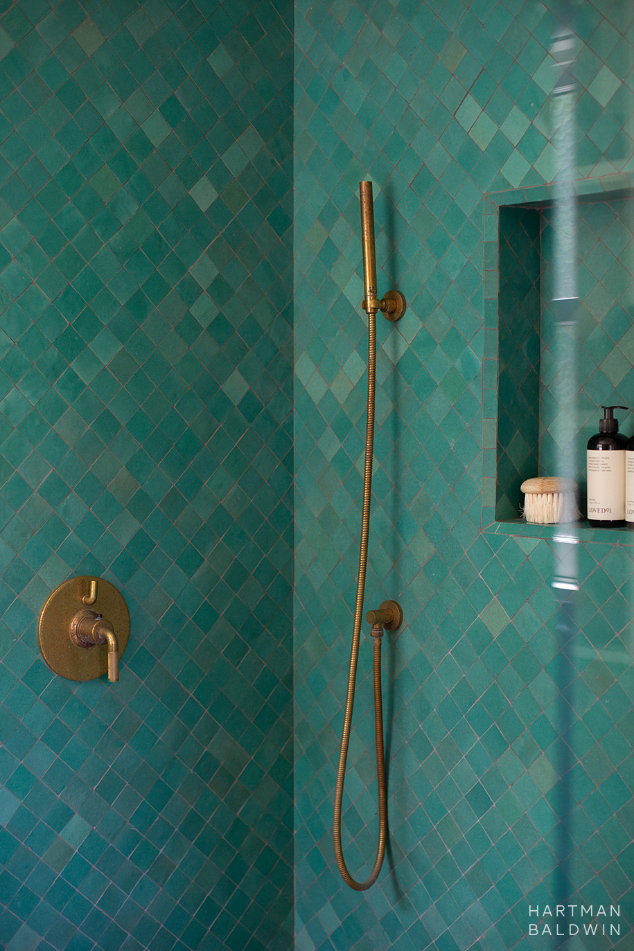 Shower detail with turquoise wall tile, niche shelf, and antique brass showerhead, handle, and hand sprayer