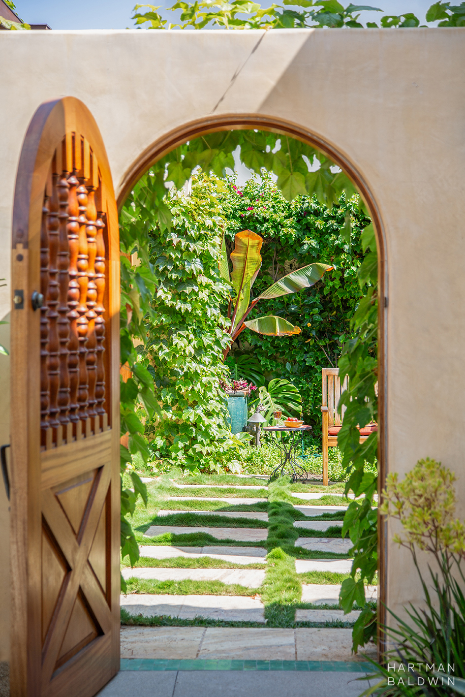 New stucco garden wall with a wooden gate open to a lush green backyard