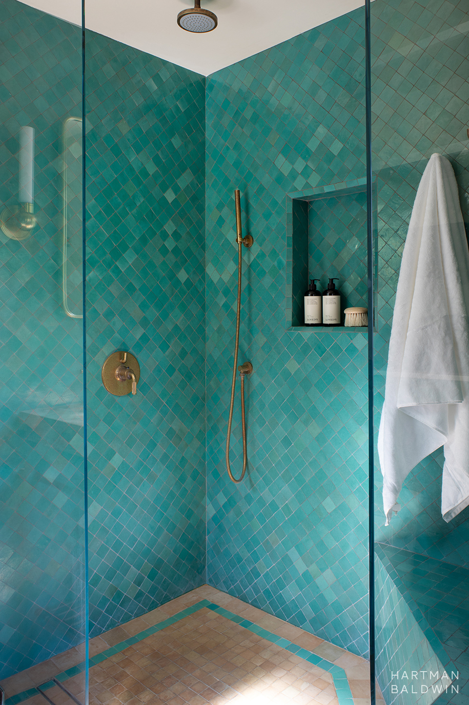 Bathroom shower with turquoise wall tile, niche shelf, and antique brass showerhead, handle, and hand sprayer
