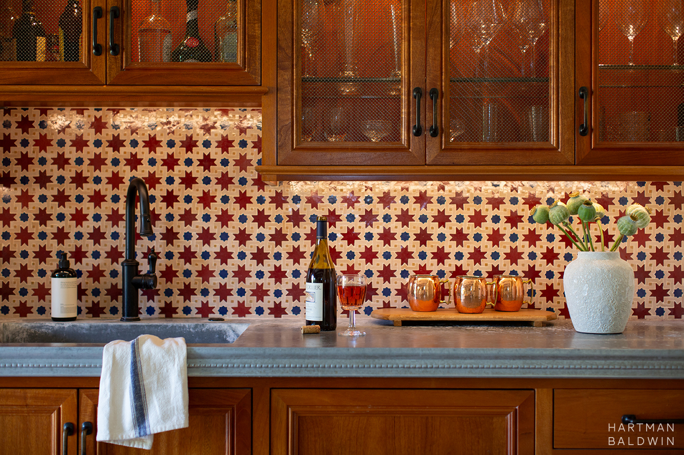 New bar counter with patinaed zinc countertop, red, cream, and blue Moroccan Mosaic tile backsplash, and wood cabinetry with mesh screens