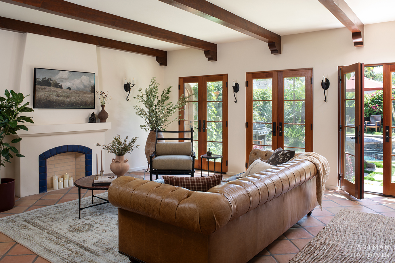 Remodeled Spanish-style living room with faux fireplace, stained wood French doors and ceiling beams, and large leather couch