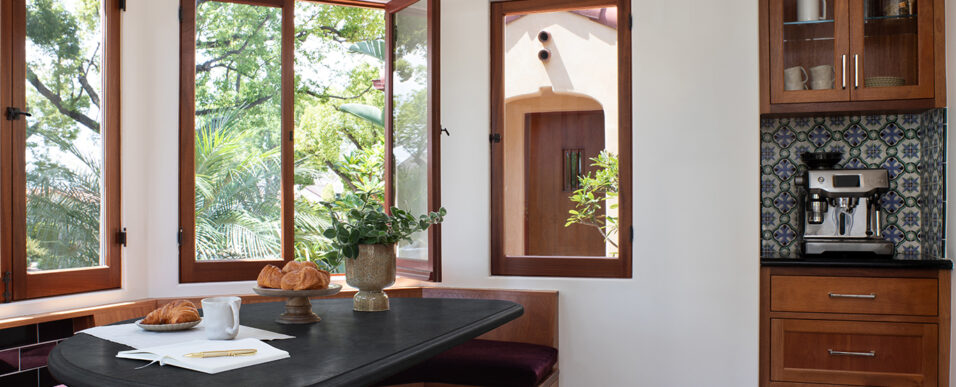 Spanish-style breakfast room with built-in banquette and table, coffee nook, and windows framing home exterior architecture and landscaping