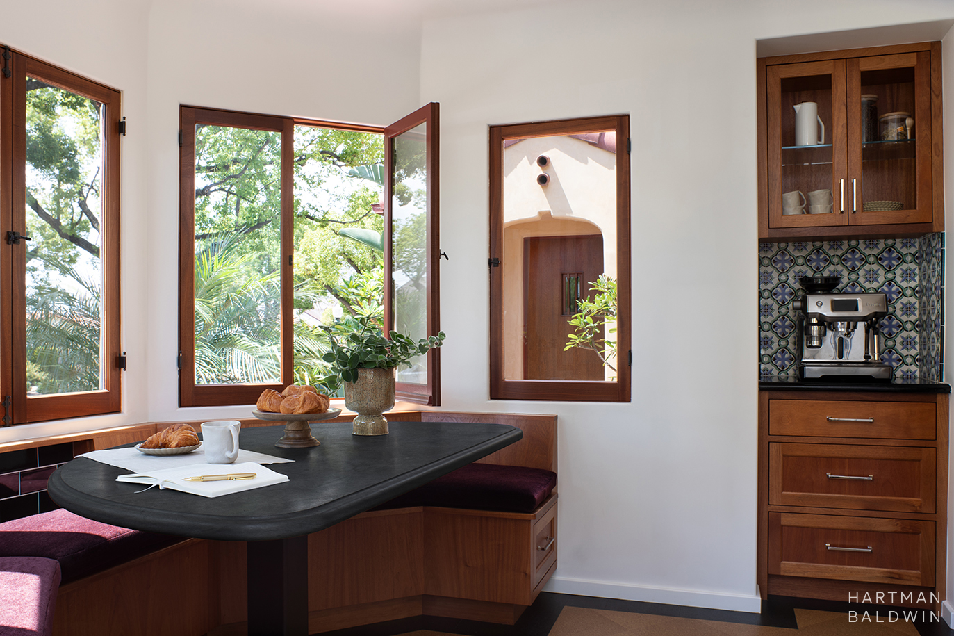Spanish-style breakfast room with built-in banquette and table, coffee nook, and windows framing home exterior architecture and landscaping