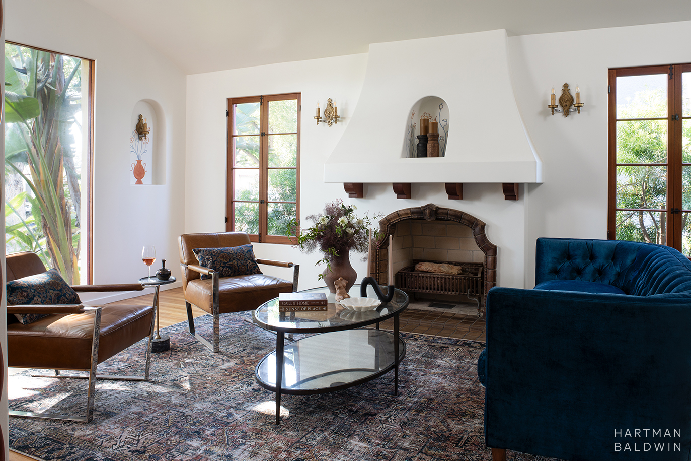 Remodeled Spanish-style living room with a fireplace, arched niches with painted illustrations, large picture window, and blue velvet couch