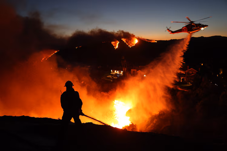 Getty Images Los Angeles Wildfire Fighting - Hartman Baldwin Pre-Launch Firefighter's silhouette in front of wildfire glow with helicopter dropping fire retardant over neighborhood and hills burning in the distance
