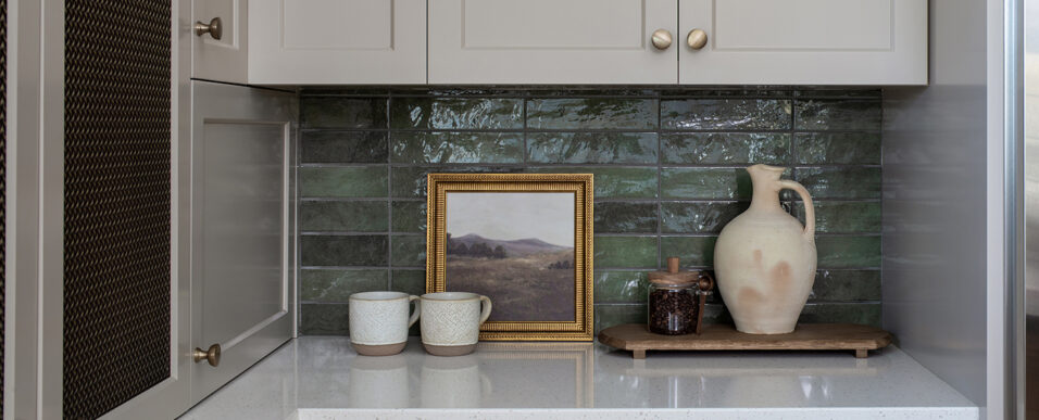 Contemporary ranch kitchen remodel corner detail with tan painted cabinetry, brass hardware, dark teal tile backsplash, and kitchen accessories