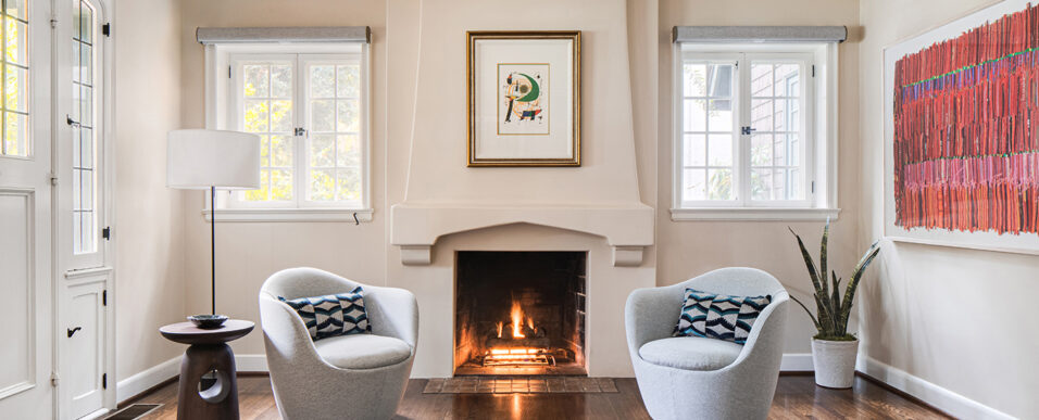 Remodeled living room with a lit fireplace and modern furnishings and abstract colorful art pieces