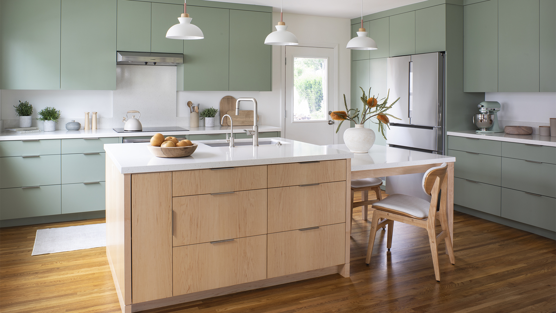 Contemporary Scandinavian minimalist style kitchen remodel with sage green cabinetry, sculptural pendant lights, and central island with built-in dining table