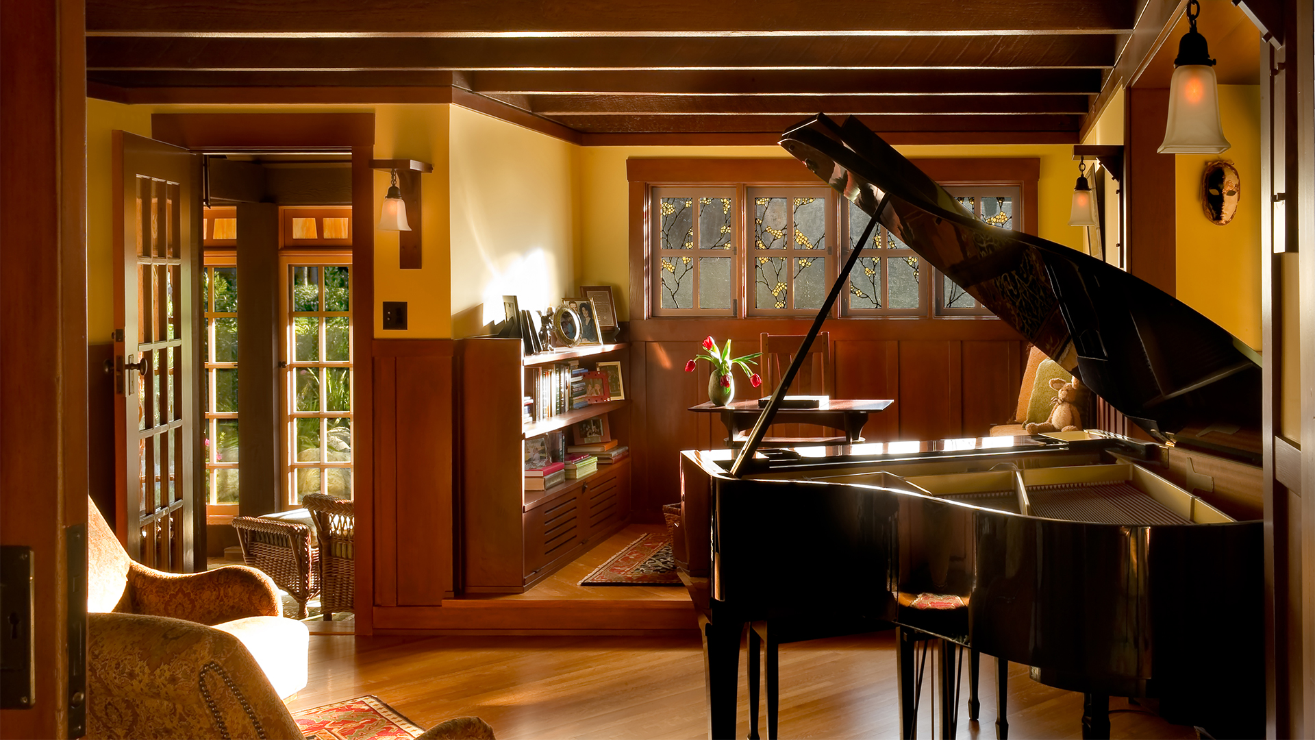 Craftsman-style living room at golden hour with grand piano, stained glass windows, built-in cabinetry, comfortable seating, and wood beams and wainscoting