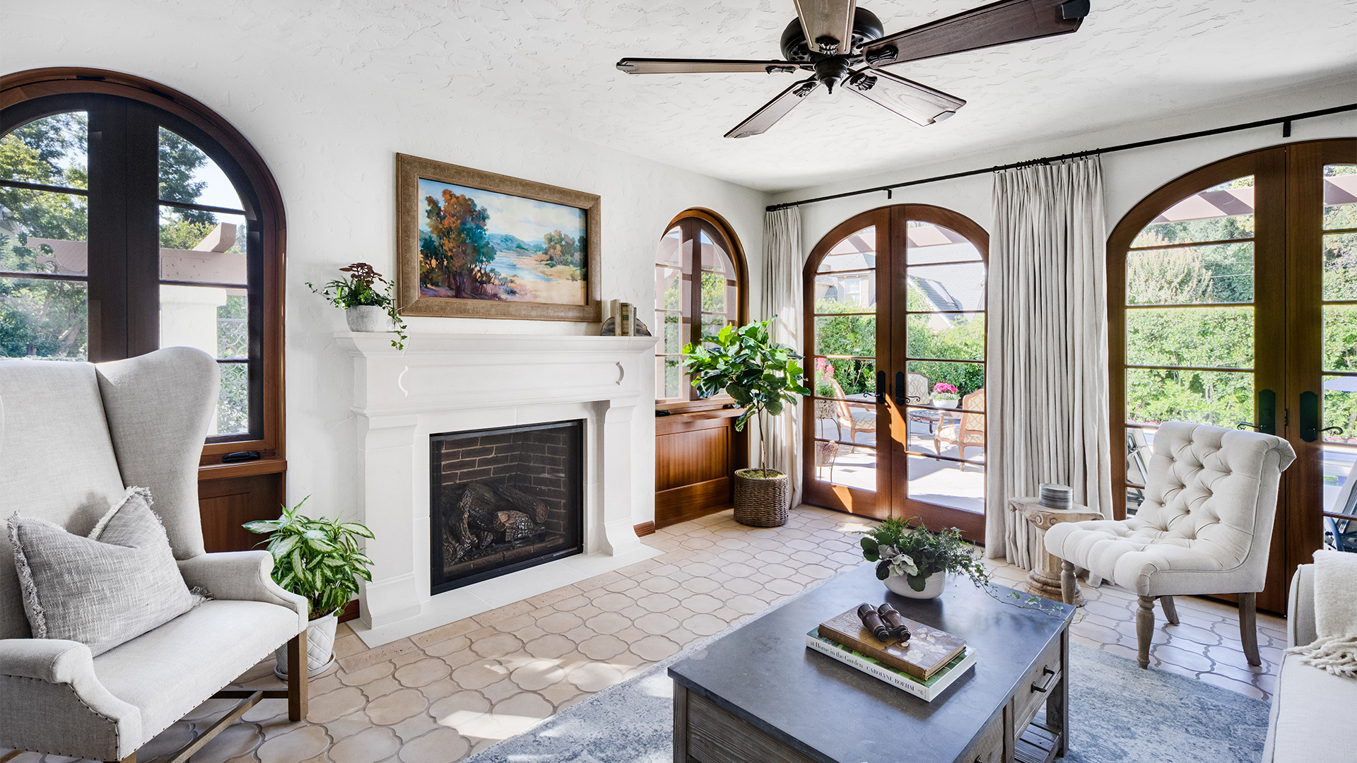 Remodeled Spanish-style sun room with arched wooden doorways and windows, white fireplace, and geometric tile floor