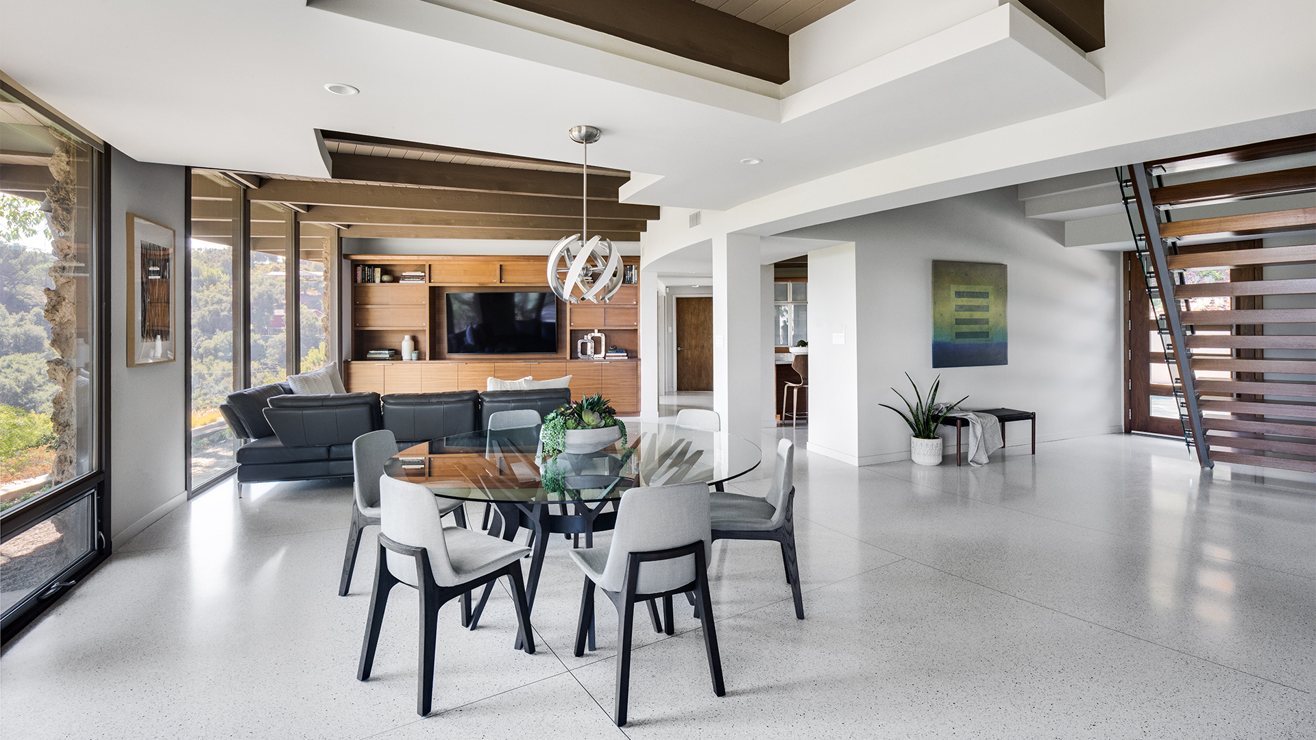 Remodeled Mid-Century Modern home open living space with entryway and floating wood stairs, round glass dining table, living room with built-in entertainment cabinet